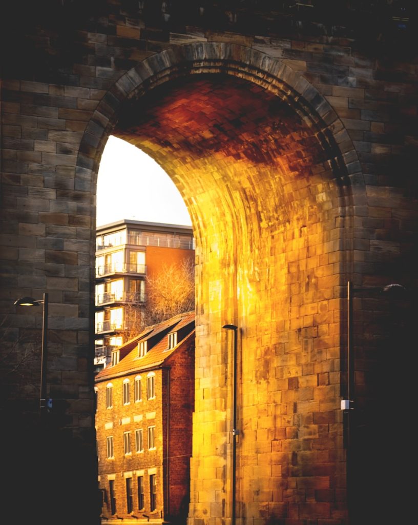 an arch in a brick wall with a building in the background